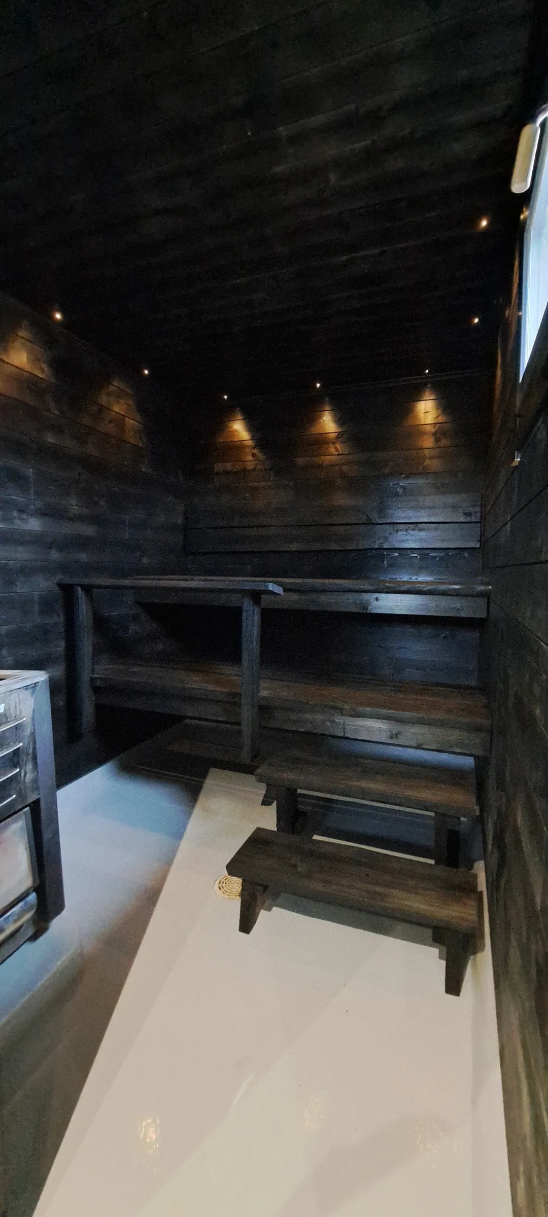 Sauna tummalla puulla, penkit ja valaistus luovat tunnelman.
